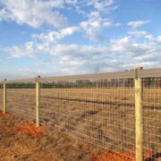 a mesh fence with a tan vinyl fence top rail in a field in Autumn