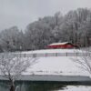 snowy field with a fence running through the middle of the filed and a large barn in the background