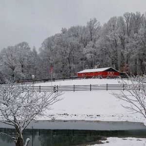 snowy field with a fence running through the middle of the filed and a large barn in the background