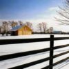 brown fence in a snow field with a tan barn in the background