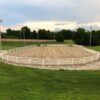 large oval white fence bordering a dirt field