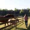 lady rancher staring next to a 4 rail fence with a horse and foal next to her