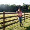 lady rancher staring next to a 4 rail fence