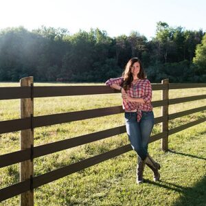 lady rancher staring next to a 4 rail fence
