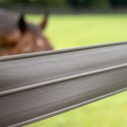 Extreme close up of a brown rail of 525 Flex Fence with a brown horse out of focus in the background