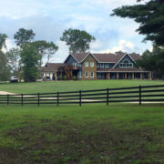 a 4 rail 525 flex fence crossing a green field with a large luxury home in the background.