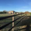 a 3 rail brown 525 flex fence installed on light tan poles in a green field with a large tan home in the background.