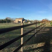 a 3 rail brown 525 flex fence installed on light tan poles in a green field with a large tan home in the background.