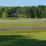 white fence at a distance with two roads in the foreground and a large luxury home in the background