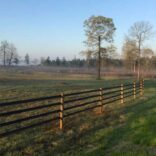 a four rail fence in the foreground of a misty field