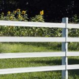 a close up of a white 4 rail fence with sunflowers in the background