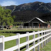 white fence in front of a barn with a mountain in the background