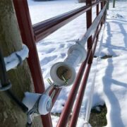 white gate handle shown securing a red farm gate closed
