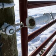 white gate handle shown securing a red farm gate closed