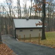 coated wire fence along a asphalt driveway next to a tan stable