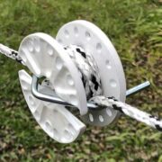 a strand of white and black braided electric fence strung through a rope tightener