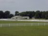 White fence in a green field with a large white stable in the background